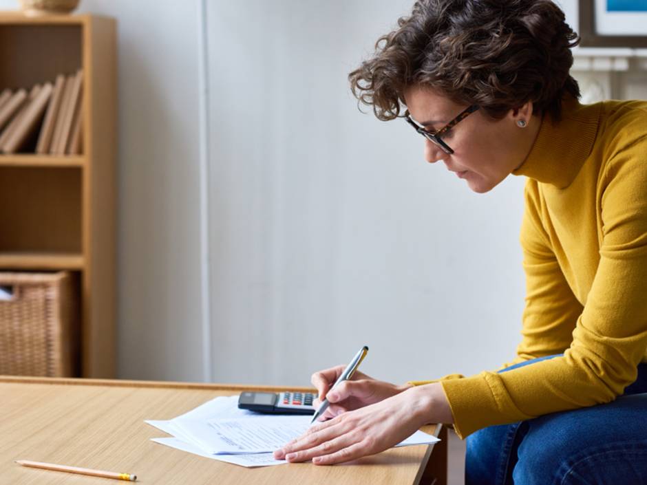 Nebenkostenabrechnung prüfen, Frau sitzt mit Taschenrechner an einem Tisch und rechnet, Foto: iStock/mediaphotos
