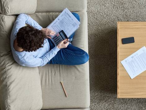 Mietzinsreduktion, Mann mit Taschenrechner auf dem Sofa, Vogelperspektive, Foto: iStock / mediaphotos